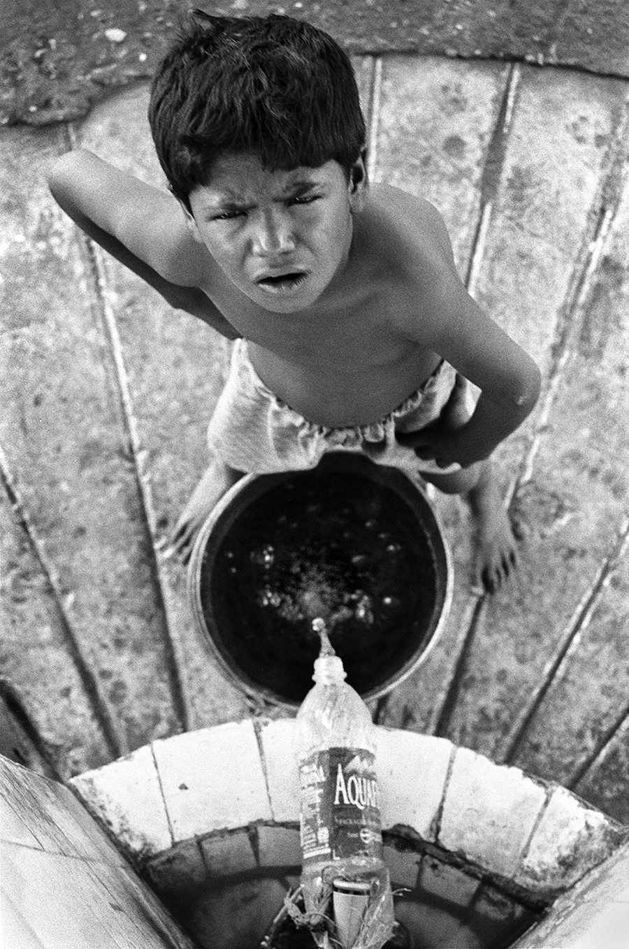 WATER FROM A BOTTLE: A young rag-picker takes a break from sifting through refuse and collects water for his bath